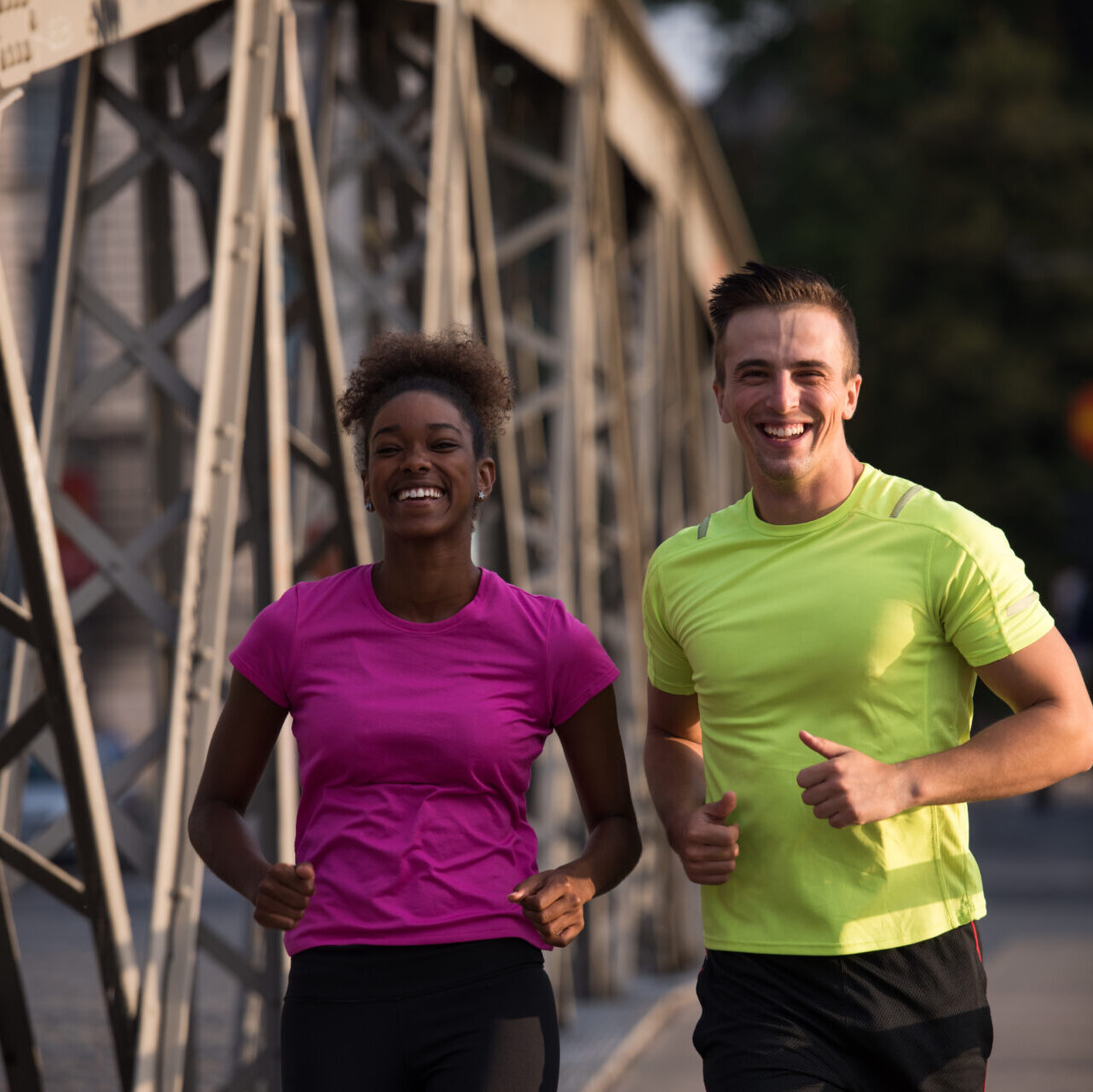 healthy young multiethnic couple jogging across the bridge in the city at early morning with sunrise in background